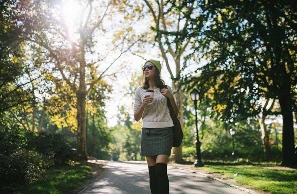 woman walking in a park drinking coffee as part of a healthy lifestyle routine